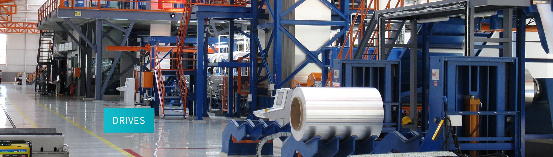Interior of an industrial facility with large rolls of metal and machinery for processing.