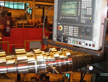 Close-up of a CNC machine drive system undergoing a retrofit, with a control panel displaying settings and a partially machined component.